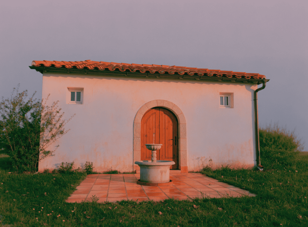 Cream Stucco - Small Homes USA Newsletter Small cottage with arched door and fountain in front, scenic outdoor setting.