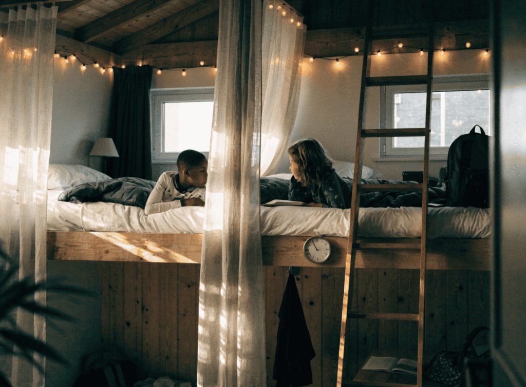 Kids Shared Loft - Small Homes USA Newsletter Two children playing on a cozy loft bed with string lights in a tiny home.